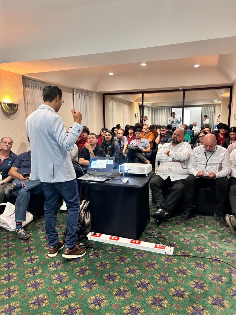 Sala de conferencias llena con ponente y audiencia atenta